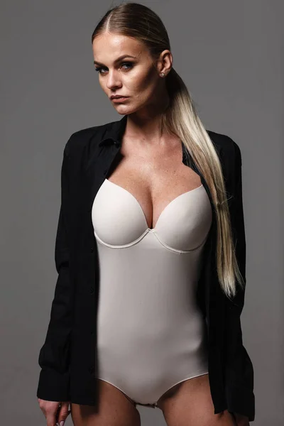 Mode och underkläder koncept - vacker blond dam porträtt i sexig naken färg korsett och svart skjorta på grå bakgrund. Kvinna bär underkläder poserar i studioljus — Stockfoto