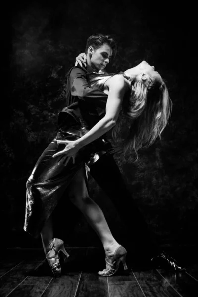 Dans en liefde concept. Jong stel in elegante avondjurken in kamer gevuld met dramatisch licht. Twee dansers man en vrouw die elkaar in een gepassioneerde houding vasthouden. Zwart-wit, monochroom — Stockfoto
