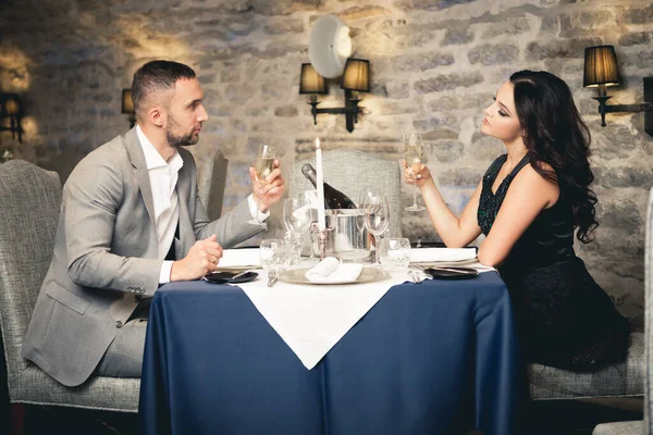 Romance e namoro conceito. Jovem casal homem e mulher com taças de champanhe comemorando e brindando no restaurante. Duas pessoas macho e fêmea em elegante terno de noite e vestido em jantar romântico — Fotografia de Stock