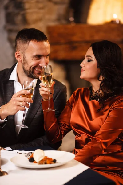 Romance e namoro conceito. Jovem casal homem e mulher com taças de champanhe comemorando e brindando no restaurante. Duas pessoas macho e fêmea em elegante terno de noite e vestido em jantar romântico — Fotografia de Stock