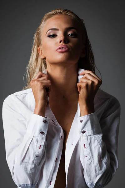 Portret van blonde jonge vrouw met mooie make-up en kapsel in wit shirt staat op grijze achtergrond. Fashion model poseert in elegante kleding in de studio — Stockfoto