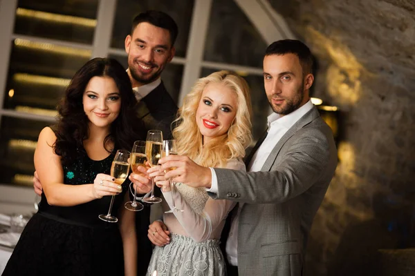 Festa, férias com amigos conceito. Quatro pessoas com taças de champanhe comemorando e brindando no restaurante. Dois homens e duas mulheres em roupas elegantes da noite, ternos e vestidos noite fora dentro de casa — Fotografia de Stock