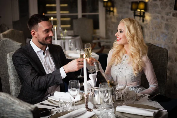 Romance e namoro conceito. Jovem casal homem e mulher com taças de champanhe comemorando e brindando no restaurante. Duas pessoas macho e fêmea em elegante terno de noite e vestido em jantar romântico — Fotografia de Stock