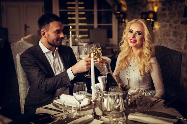 Romantik och dejting koncept. Unga par man och kvinna med champagneglas firar och skålar i restaurang. Två personer man och kvinna i elegant aftonkostym och klänning på romantisk middag — Stockfoto