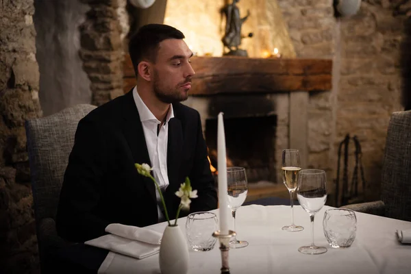 Romantyczne i randkowe pojęcie. Młody mężczyzna ze szklanką szampana na stole czeka, aż kobieta świętuje w restauracji. Przystojny mężczyzna w eleganckim stroju wieczorowym siedzi i szykuje się na romantyczną kolację — Zdjęcie stockowe