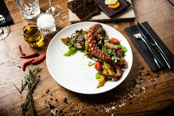 Insalata di polpo calda con verdure fritte mescolate e salsa aji su piatto bianco. Delizioso primo piano di pesce tradizionale mediterraneo sano servito su un tavolo per il pranzo . — Foto Stock