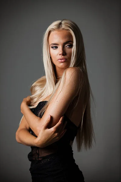 Porträt einer blonden jungen Frau mit wunderschönem Make-up und Frisur in einem schwarzen Spitzenkleid steht auf grauem Hintergrund. Modemodel posiert in eleganter Kleidung im Studio — Stockfoto