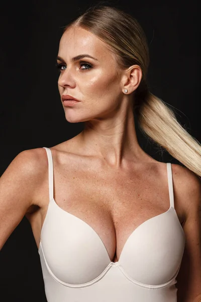 Fashion en lingerie concept - mooie blonde dame portret in sexy naakt kleur korset op zwarte achtergrond. Vrouw in ondergoed poseert in studio licht — Stockfoto