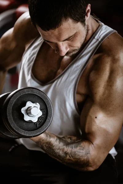 Fitness in sportschool, sport en een gezonde levensstijl concept. Knappe atletische man in wit shirt die oefeningen maakt. Bodybuilder mannelijk model training biceps spieren met halter — Stockfoto