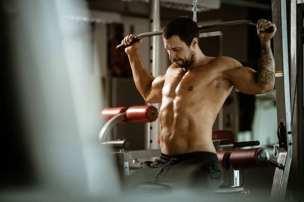 Fitness in sportschool, sport en een gezonde levensstijl concept. Knappe atletische man met naakte romp die oefeningen doet. Bodybuilder mannelijk model traint rugspieren met behulp van trainingsmachine — Stockfoto