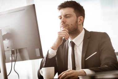 İş krizi konsepti. Ofis masasında oturan genç işadamı cep telefonuyla çok ciddi bir iş problemini çözmekle meşgul. Camdan arka planda takım elbiseli bir adam..