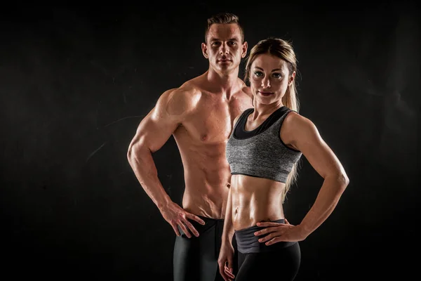 スポーツ 健康的なライフスタイルのコンセプトでフィットネス 陸上競技の男性と女性のカップルは暗い背景に彼らの訓練された体を示す 二つのボディビルダーのモデルが立っているとタイトな筋肉を実証 — ストック写真