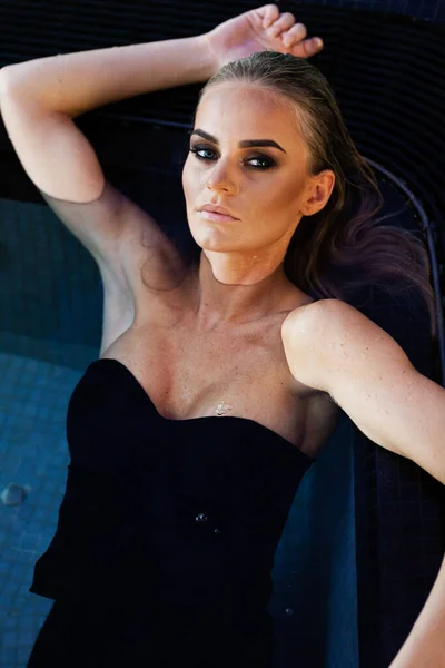 放松和温泉的概念 一个穿着黑色泳衣的性感时髦女人的画像 在自然阳光的照射下 湿头发和化妆的女人在游泳池里的水里摆姿势 — 图库照片