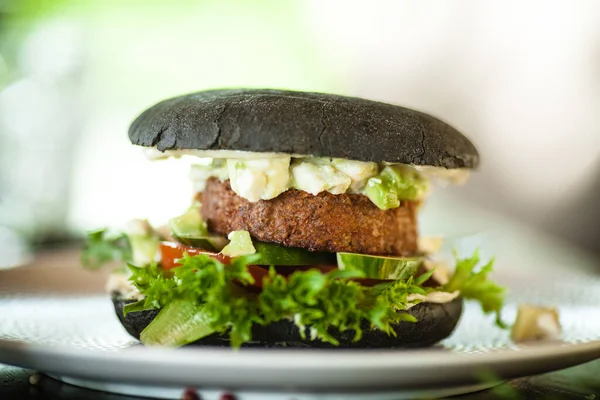Vegan burger. Black bun, tofu-avocado salad, mayonnaise, cucumber, tomato, fresh salad. Delicious healthy hamburger food closeup served on a table for lunch in modern cuisine gourmet restaurant