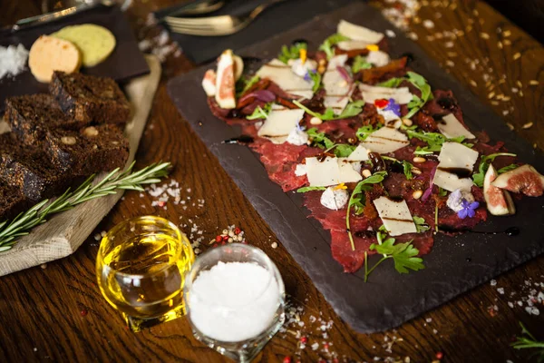 Carpaccio di manzo con pepe, rucola e parmigiano servito su una tavola. Deliziosi antipasti tradizionali italiani spuntini primi piani serviti a pranzo con vino nel moderno ristorante di cucina gourmet — Foto Stock