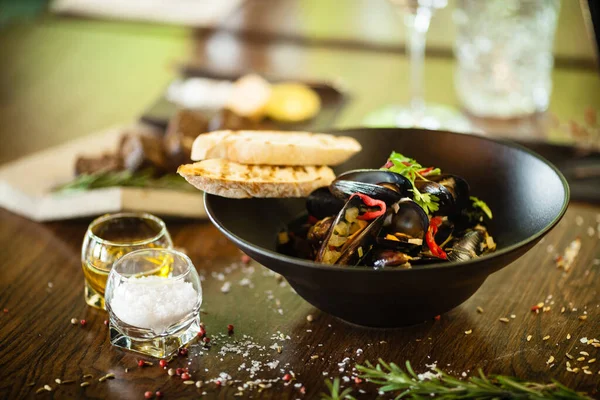 Cozze blu in salsa di vino bianco in ciotola nera. Delizioso primo piano di pesce sano servito su un tavolo per il pranzo in cucina moderna ristorante gourmet — Foto Stock