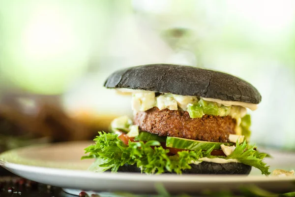 Veganský burger. Černá houska, tofu-avokádový salát, majonéza, okurka, rajče, čerstvý salát. Lahodné zdravé hamburger jídlo detailní servírované na stole k obědu v moderní kuchyni gurmánská restaurace. — Stock fotografie