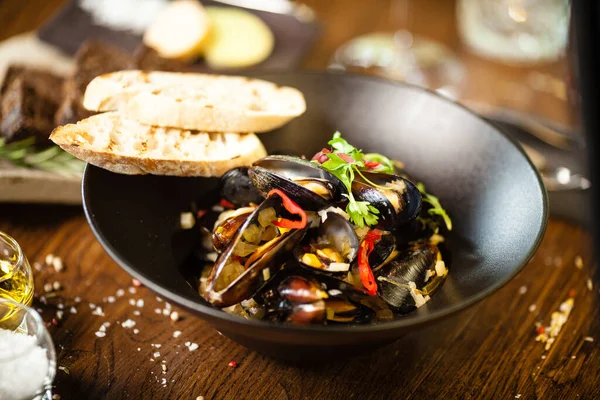 Mexilhões azuis em molho de vinho branco em tigela preta. Delicioso closeup de frutos do mar saudáveis servido em uma mesa para almoço na cozinha moderna restaurante gourmet — Fotografia de Stock