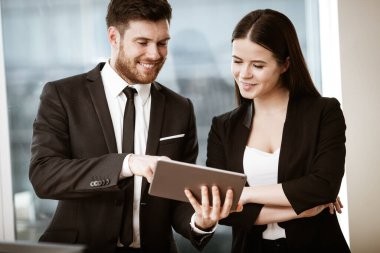 Başarılı iş ve modern teknoloji kavramı. Genç iş kadını ve mutlu gülümseyen iş adamı tablet bilgisayar kullanarak birlikte çalışıyorlar. İki meslektaş erkek ve kadın takım çalışması.