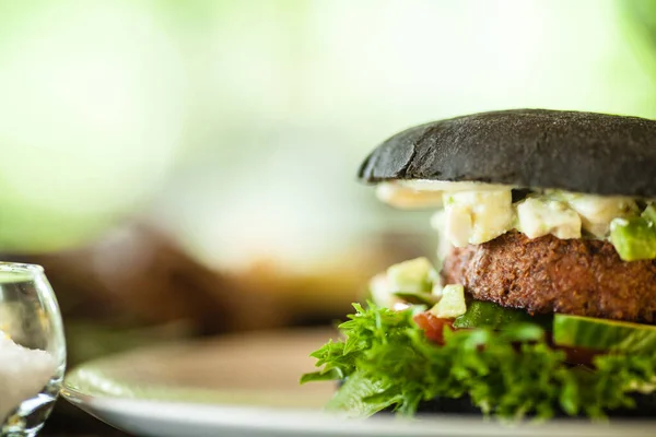 Vegan burger. Black bun, tofu-avocado salad, mayonnaise, cucumber, tomato, fresh salad. Delicious healthy hamburger food closeup served on a table for lunch in modern cuisine gourmet restaurant