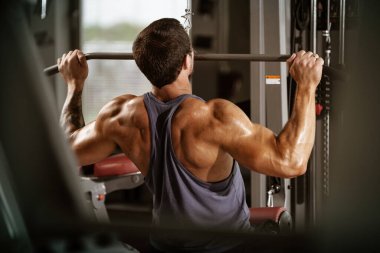 Spor, spor ve sağlıklı yaşam tarzı konsepti. Mavi gömlekli yakışıklı atletik adam egzersiz yapıyor. Vücut geliştiren erkek model egzersiz makinesi kullanarak sırt kaslarını çalıştırıyor..