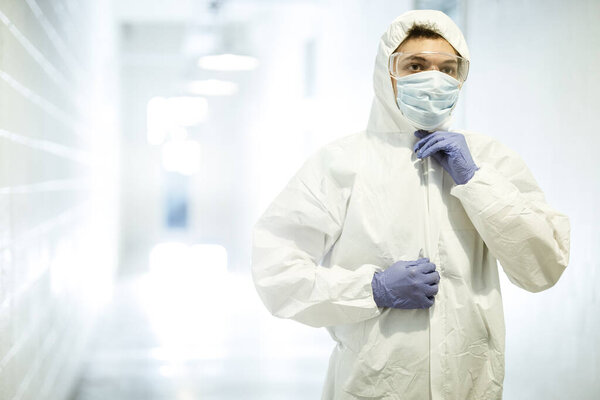 Corona virus concept. Male scientist doctor in mask, glasses and gloves puts on protective suit and getting ready for COVID pandemic outbreak quarantine. Man in biochemistry laboratory.