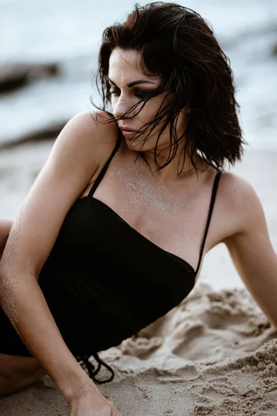 Concepto de recreación estival. Hermosa mujer sexy joven con el cuerpo delgado entrenado en forma usando bikini traje de baño negro se encuentra en una playa. Moda modelo femenino posa junto al mar — Foto de Stock