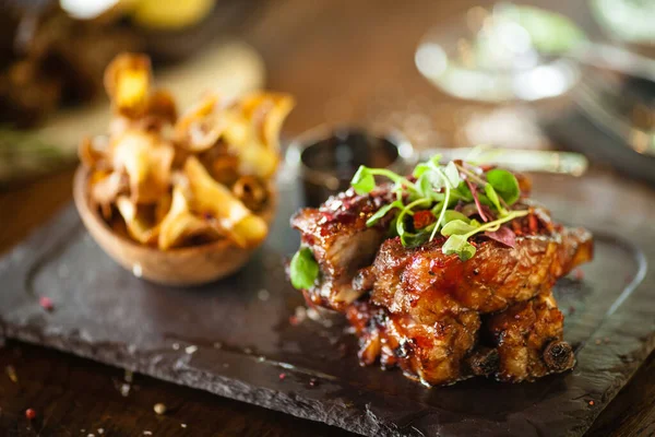 Schweinerippchen bei niedriger Temperatur gekocht. Schwarze Johannisbeersoße, Pastinakenchips mit Parmesan. Köstliche gesunde Fleischgerichte in Nahaufnahme, serviert auf einem Tisch zum Mittagessen im Gourmetrestaurant der modernen Küche — Stockfoto