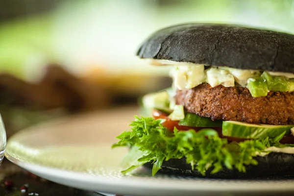 Veganer Burger. Schwarzbrötchen, Tofu-Avocado-Salat, Mayonnaise, Gurken, Tomaten, frischer Salat. Köstliche gesunde Hamburger in Nahaufnahme, serviert auf einem Tisch zum Mittagessen im Gourmetrestaurant der modernen Küche. — Stockfoto