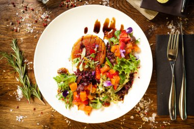 Keçi peynirli salata. Kırmızı biberli çilek-kavun salatası, elma-portakal sosu, beyaz tabakta incir reçeli. Modern yemek gurme restoranında öğle yemeği için bir masaya servis edilen lezzetli et yemekleri..