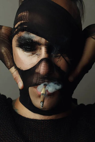 Sigara içen adamın closeup stüdyo portresi, modelyüzü kısmen çorap ile kaplıdır. Yaratıcı makyaj moda sanat tasarımı. 