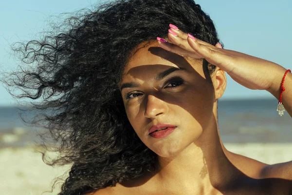 Portrait of female model at seaside with natural makeup. Close-up image of beautiful woman face with soft color lipstick. Sexy full lips. Curly hair. Golden skin. Summer vibes