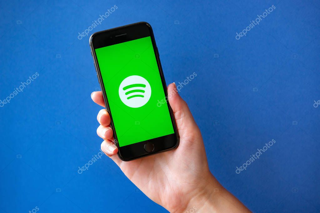 Kyiv, Ukraine - October 1, 2019: Studio shot of hand holding Apple iPhone 8 with Spotify logotype on a screen. Isolated on a blue paper background.