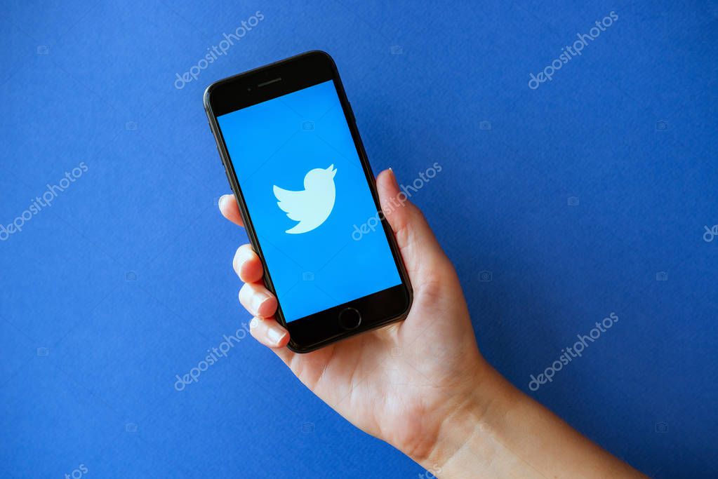 Kyiv, Ukraine - October 1, 2019: Studio shot of hand holding Apple iPhone 8 with Twitter logotype on a screen. Isolated on a blue paper background.