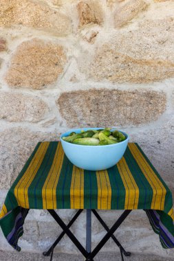 Bir kase yeşil sebze altında çizgili bir bez olan bir masada oturur. Kase brokoli ve diğer yeşil sebzelerle dolu ve masa ahşaptan yapılmış.