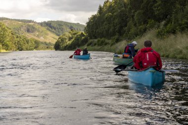 İskoçya, Birleşik Krallık, 4 Ağustos 2025: Üç kişi bir nehirde kürek çekiyor. Su sakin ve gökyüzü bulutlu..