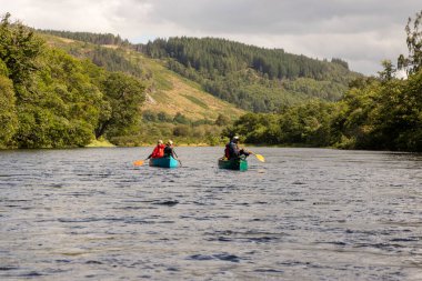 İskoçya, Birleşik Krallık, 4 Ağustos 2025: İki kişi bir nehirde kürek çekiyor. Su sakin ve gökyüzü bulutlu..