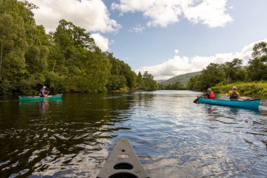 İskoçya, Birleşik Krallık, 4 Ağustos 2025: Bir grup insan bir nehirde kano çırpıyor. Su sakin ve gökyüzü berrak..