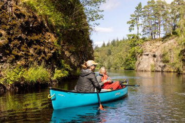 İskoçya, Birleşik Krallık, 4 Ağustos 2025: Bir erkek ve bir kadın bir nehirde mavi bir kanodalar. Kadınlar kürek çekiyor..