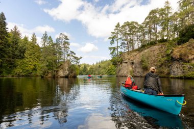 İskoçya, Birleşik Krallık, 4 Ağustos 2025: Bir grup insan bir gölde mavi bir kanoda. Su sakin ve gökyüzü berrak..