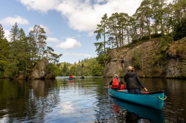 İskoçya, Birleşik Krallık, 4 Ağustos 2025: Bir grup insan bir nehirde mavi bir kanoda. Su sakin ve gökyüzü berrak..