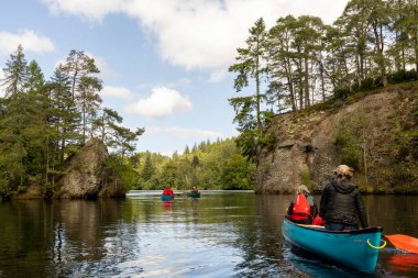 İskoçya, Birleşik Krallık, 4 Ağustos 2025: Bir grup insan bir göl üzerinde kano çırpıyor. Su sakin ve gökyüzü berrak..