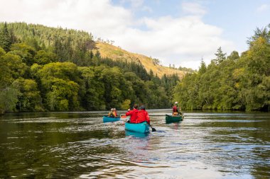 İskoçya, Birleşik Krallık, 4 Ağustos 2025: Bir grup insan bir nehirde kürek çekiyor. Su sakin ve gökyüzü bulutlu.