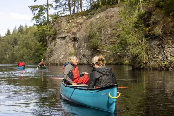 İskoçya, Birleşik Krallık, 4 Ağustos 2025: Bir grup insan bir nehirde mavi bir kanoda. Manzara huzurlu ve rahatlatıcı..