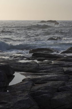 Okyanus sakin ve gökyüzü mavinin güzel bir tonu. Kıyıdaki kayalar büyük ve pürüzlü. Bu da dayanıklılık ve dayanıklılık hissi yaratıyor. Su durgun, dalgalar ve dalgalar yok.