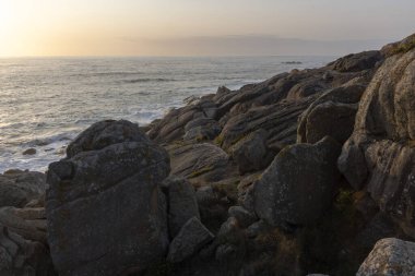 Okyanus sakin ve gökyüzü güzel turuncu bir renktir. Kayalar büyük ve su koyu mavi.