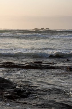 Okyanus sakin ve gökyüzü güzel turuncu bir renktir. Su temiz ve kayalar sahnenin her tarafına dağılmış.