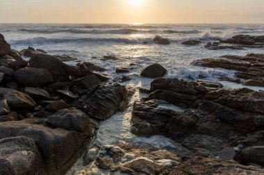 Okyanus sakin ve güneş batıyor. Kıyı şeridine dağılmış kayalar güzel ve huzurlu bir manzara yaratıyor.