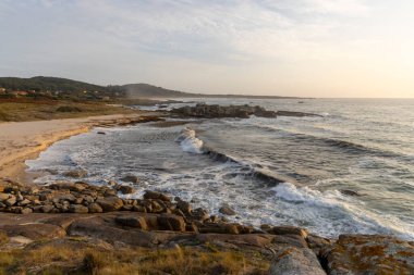 Okyanus sakin ve gökyüzü bulutlu. Kumsal kayalık ve su koyu mavi.