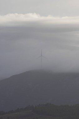 Arka planda bulutlu bir gökyüzü olan bir rüzgar türbini uzaktan görülebilir. Sakin ve dinginlik kavramı, rüzgarın türbini bulutlu gökyüzünün arka planına karşı dimdik ve gururlu duruyor.
